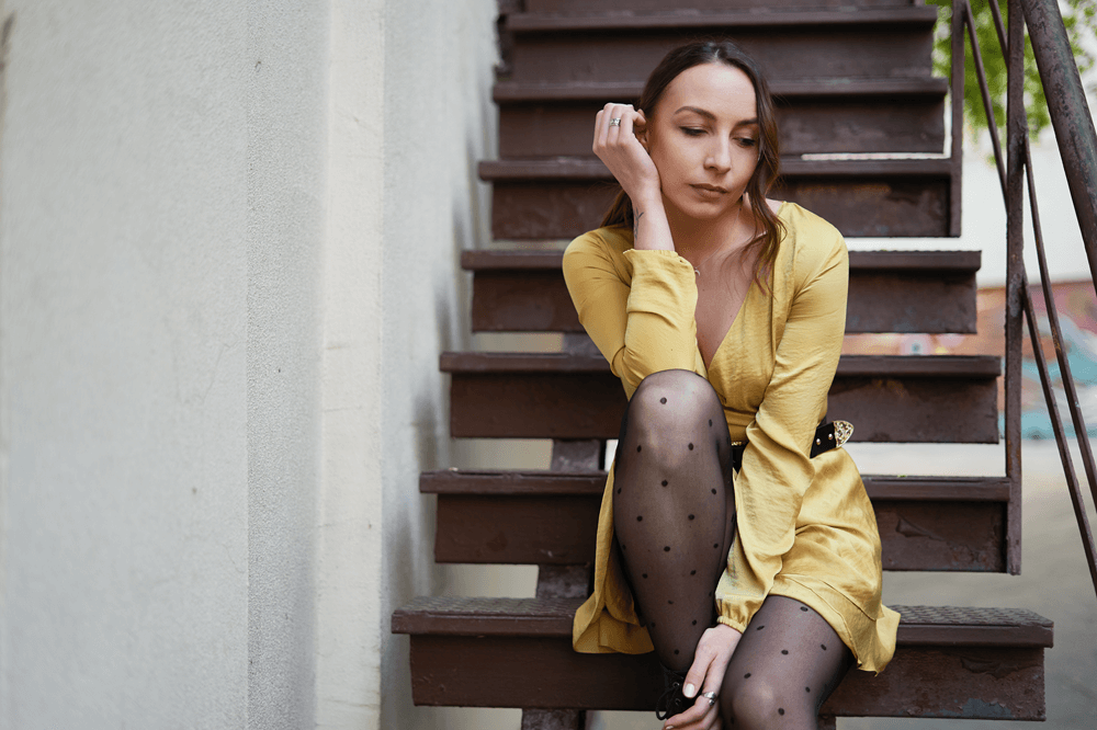 Stylish woman in sheer black tights and sneakers sitting on a stool in a cozy loft.