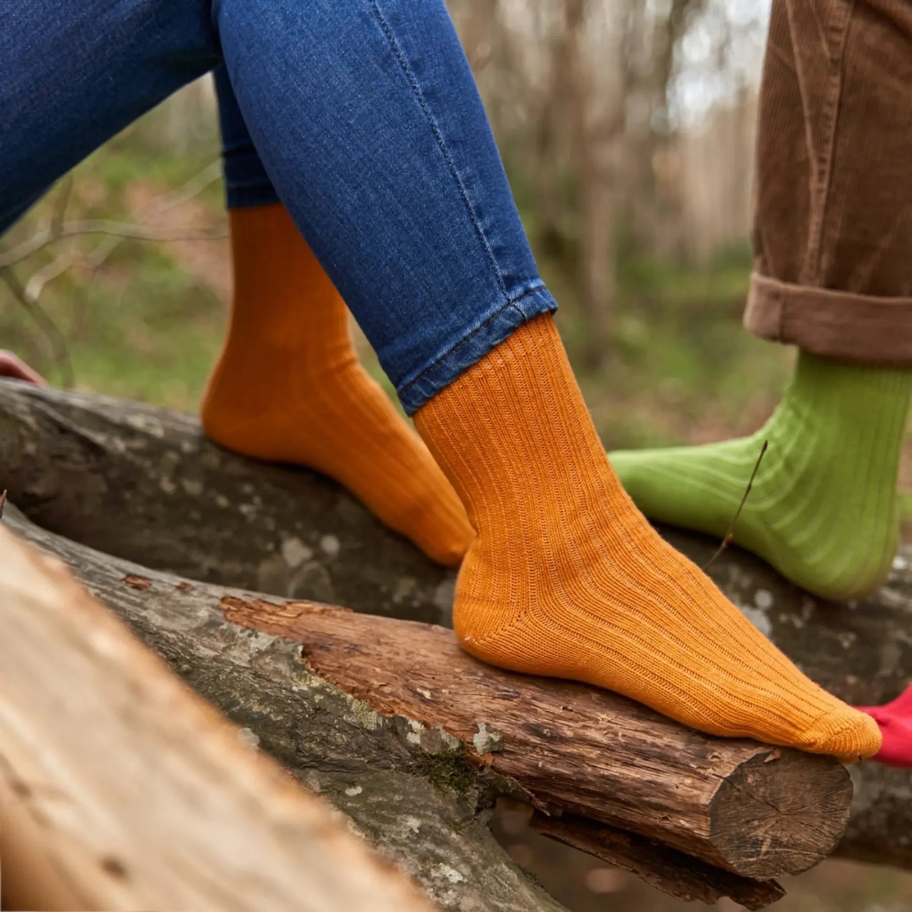 Person wearing orange bio-cotton socks sitting on a tree trunk