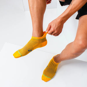 Male athlete putting on an orange bamboo running sock, demonstrating the elastic heel tab grip and secure anatomical fit