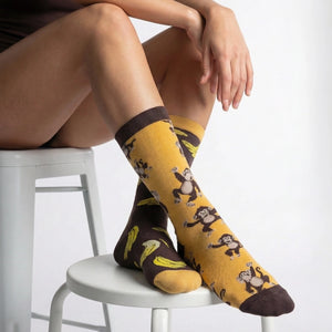 Person wearing mismatched brown socks with monkey and banana patterns sitting on a white stool