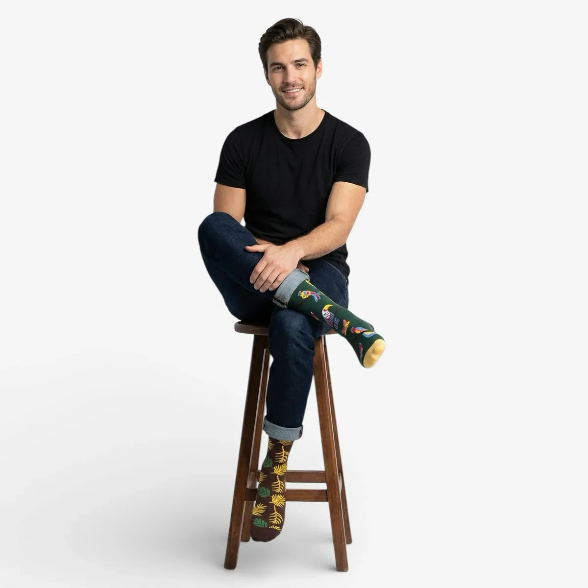 Man sitting on a stool wearing mismatched bird themed socks against a white background