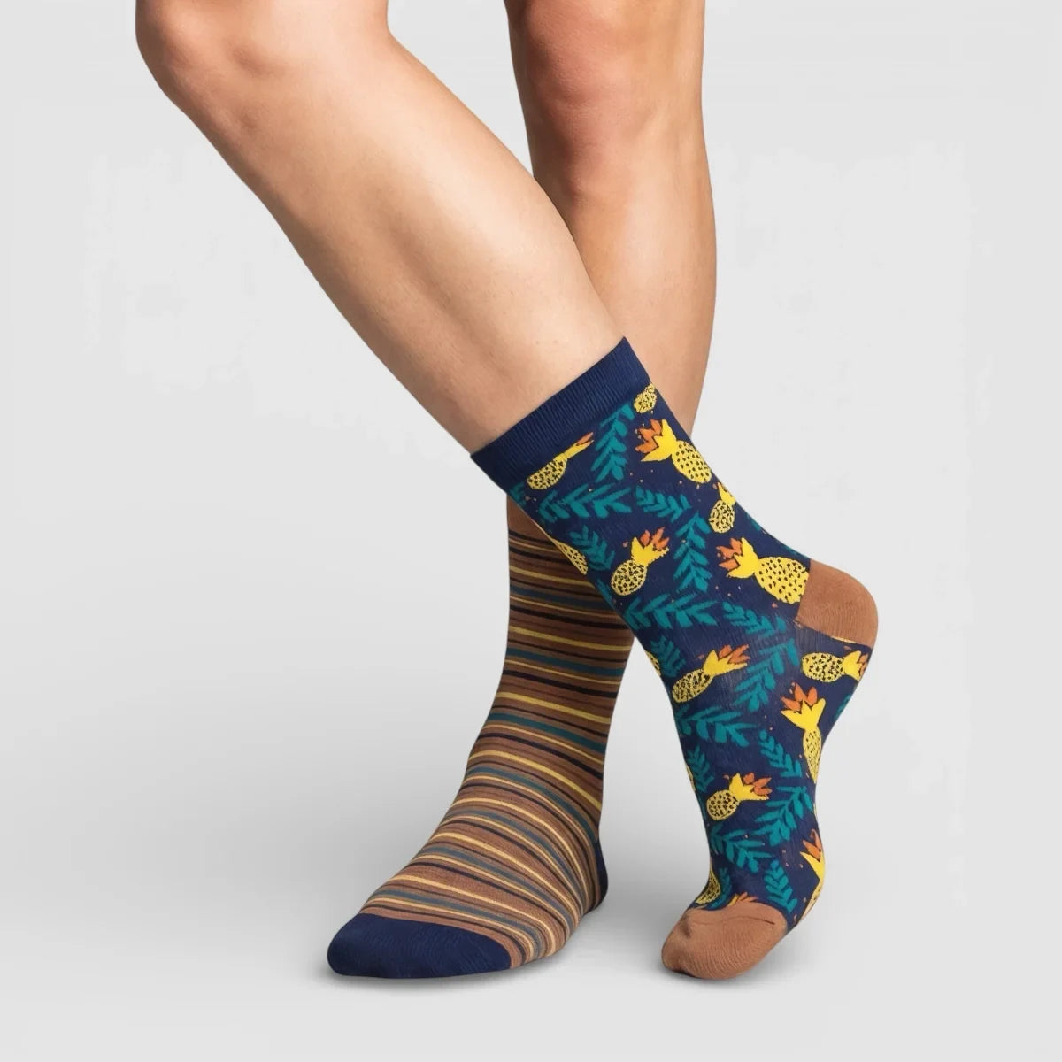 Mismatched socks, one with a striped pattern and the other with a pineapple design, on a light grey background.