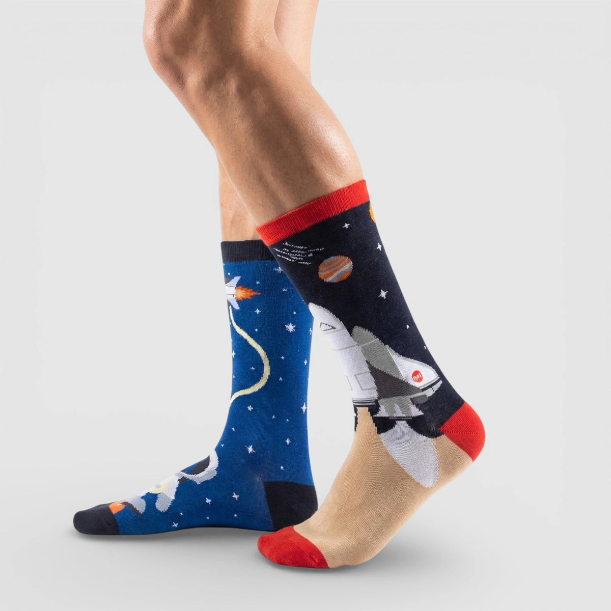 Mismatched space-themed socks with astronauts and rockets on a plain background