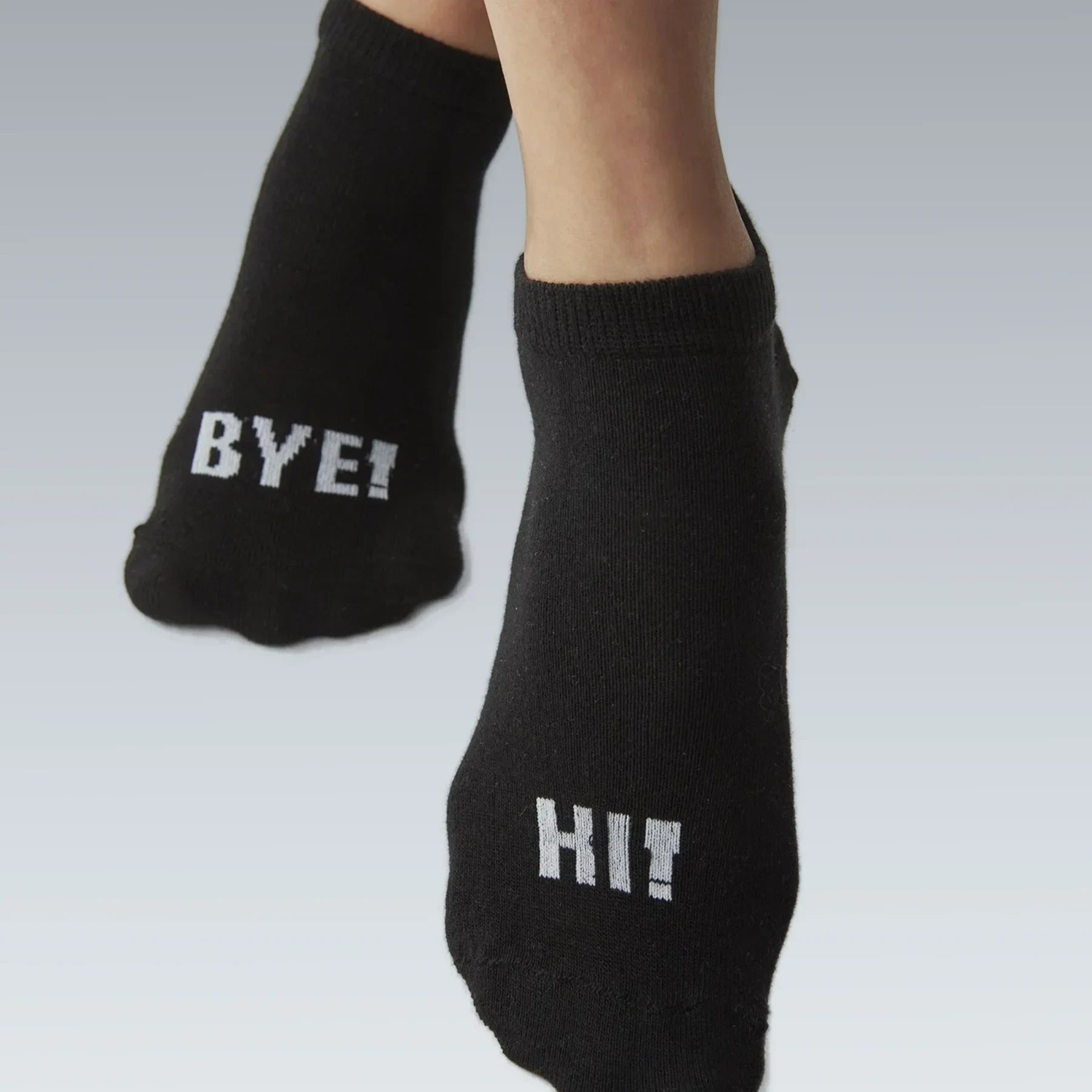 Person wearing black socks with the right foot stating Hi! and the left foot stating Bye!