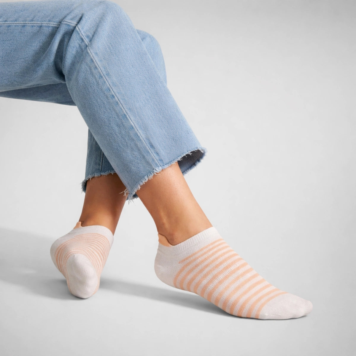 Person wearing light blue jeans and white and coral striped socks on a light background