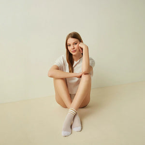 woman wearing white with beige striped open-weave socks on a light background