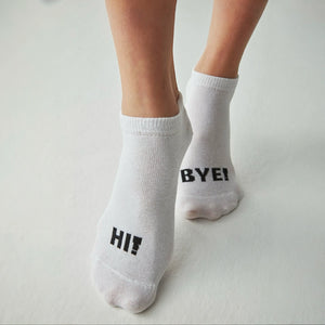 Person wearing white socks with the right foot stating Hi! and the left foot stating Bye!