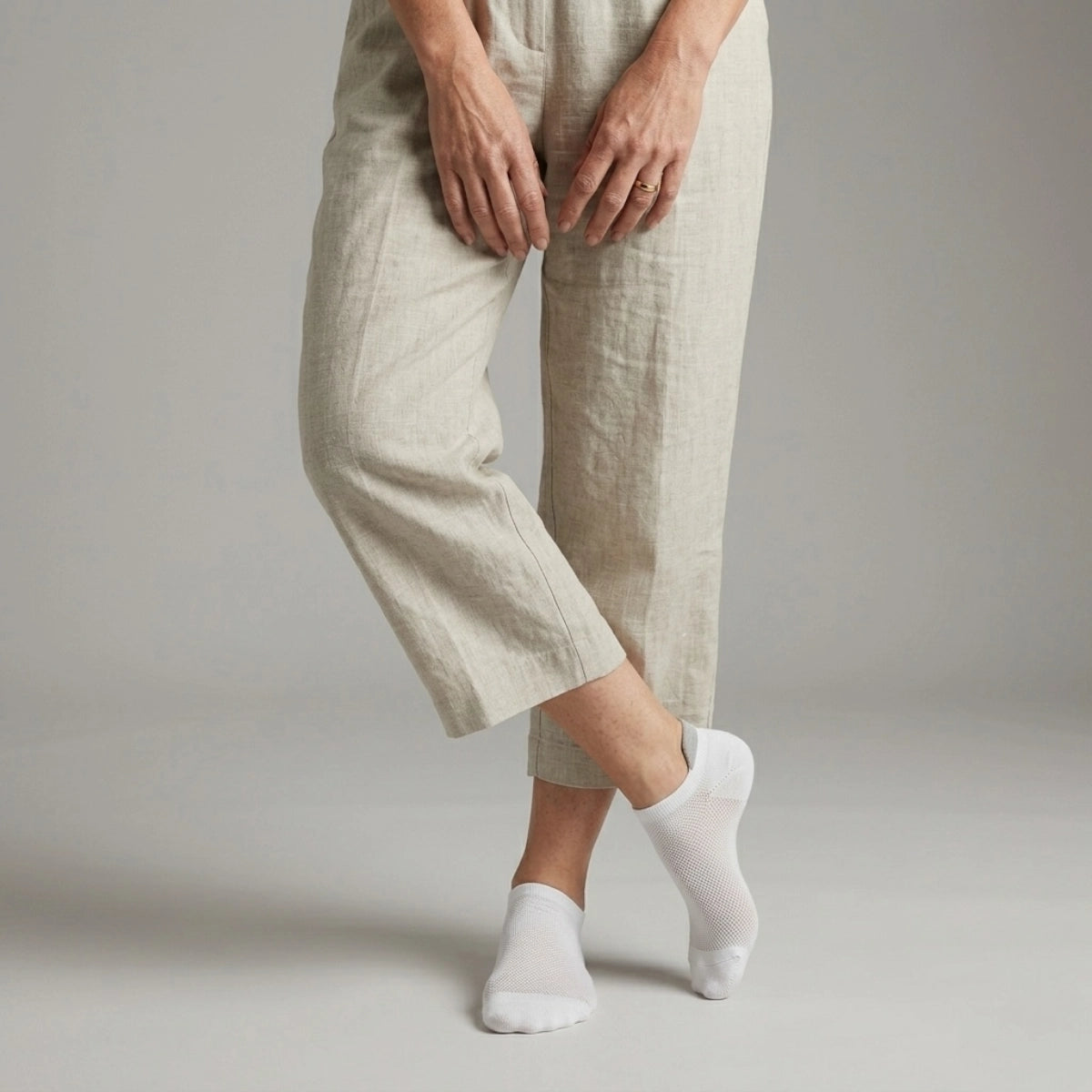 Person wearing beige pants and white socks with grey heel tab against a plain background