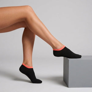 Person wearing black seamless ankle socks with orange cuff against a neutral background