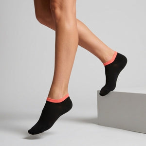 Person wearing black seamless ankle socks with orange cuff against a neutral background