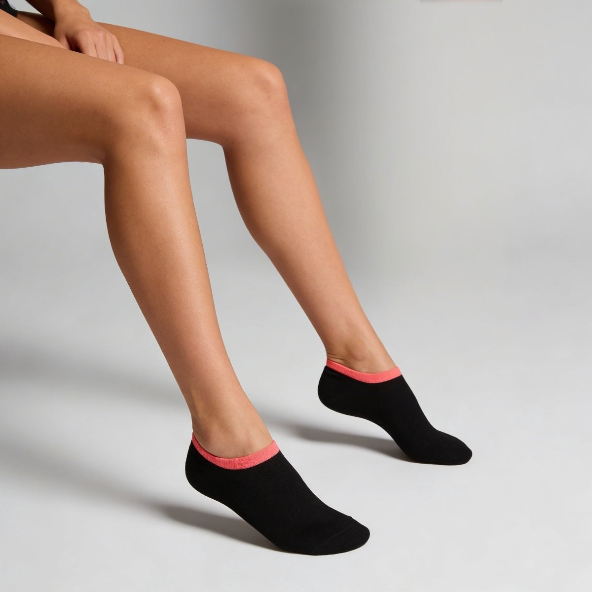 Black ankle socks with pink trim worn by a person on a grey background