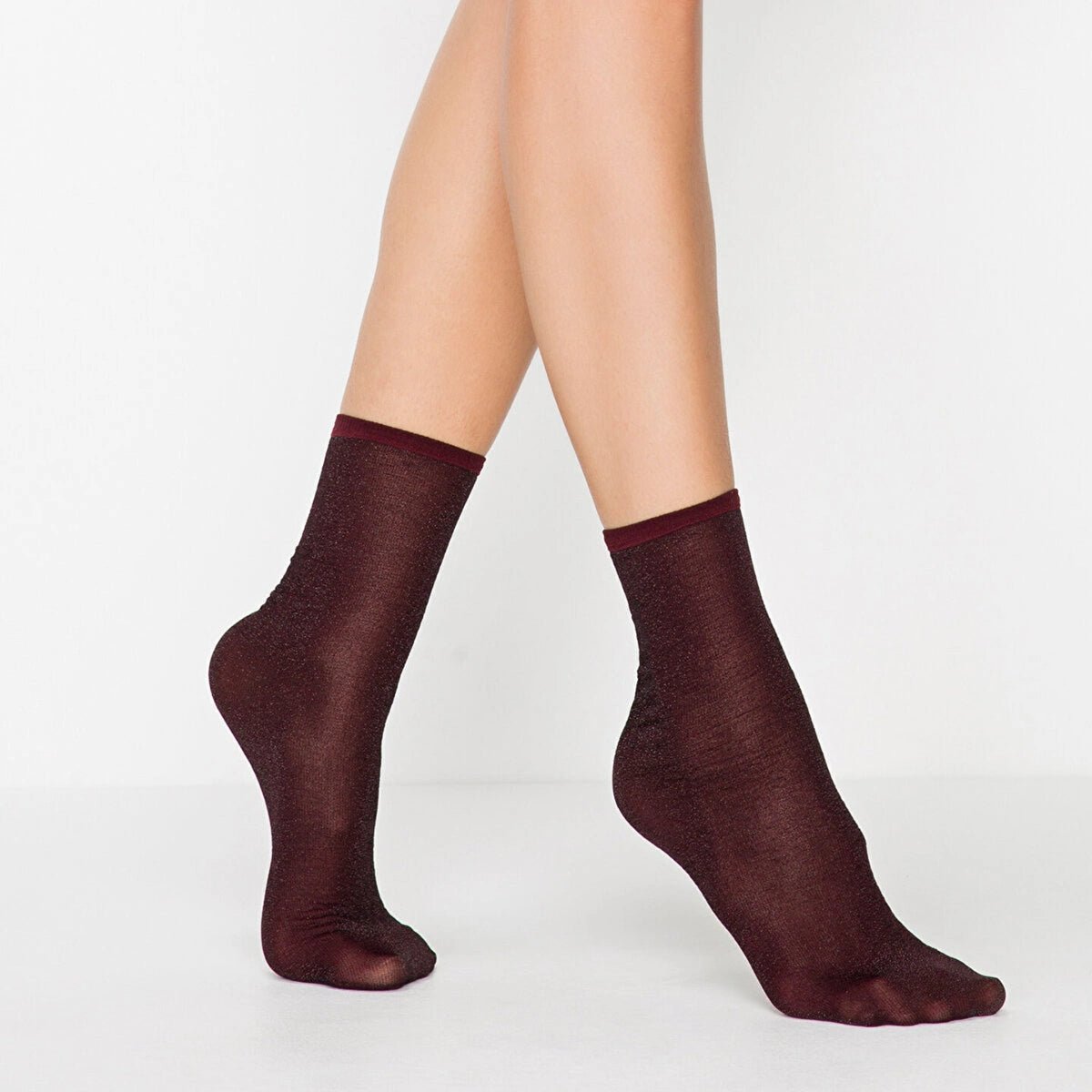 Woman wearing burgundy sparkly ankle socks with a ribbed cuff, feet crossed at the ankle