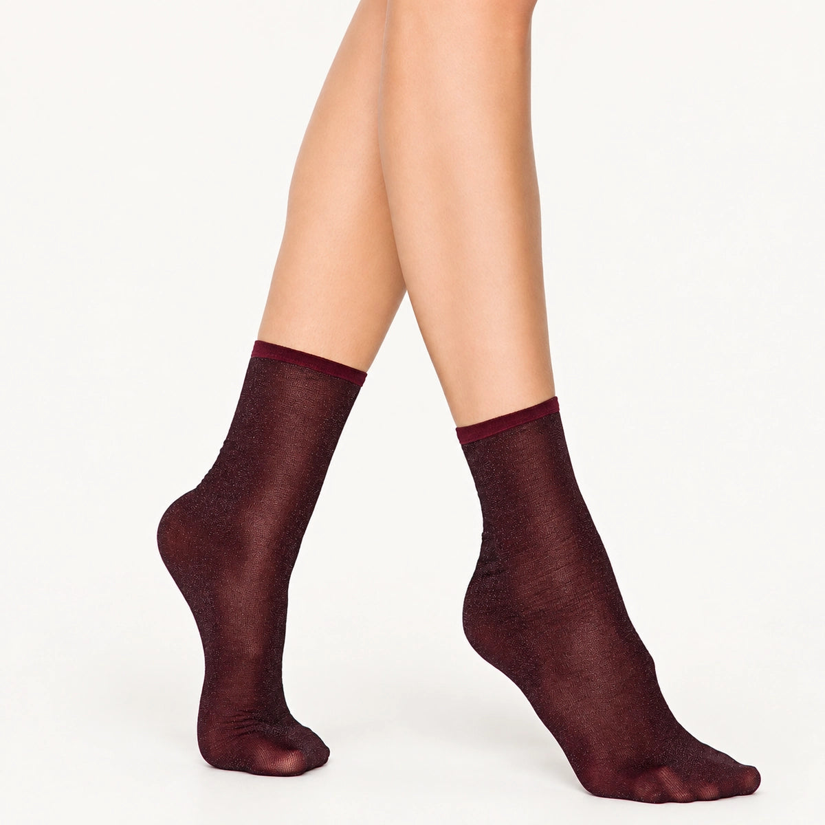 Woman wearing burgundy sparkly ankle socks with a ribbed cuff, feet crossed at the ankle