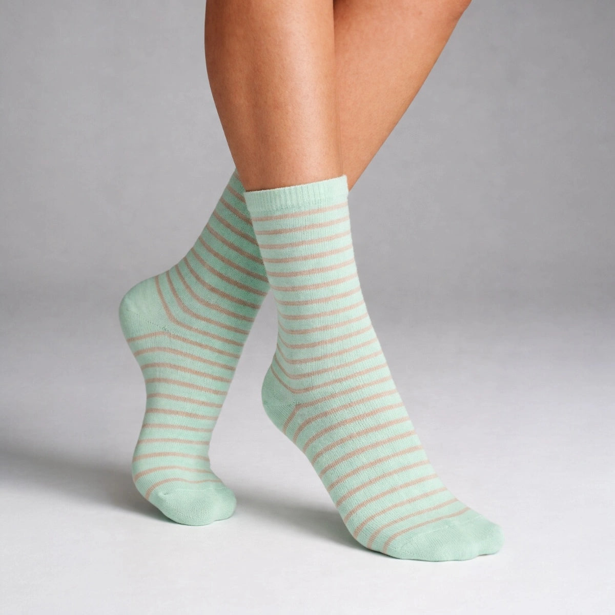 A person wearing mint socks with thin sheer stripes on a grey background