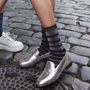 Person wearing silver loafers and silver and black striped striped socks on a cobblestone street.