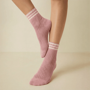 Pink open-weave socks with white striped cuff socks worn by a person on a light background