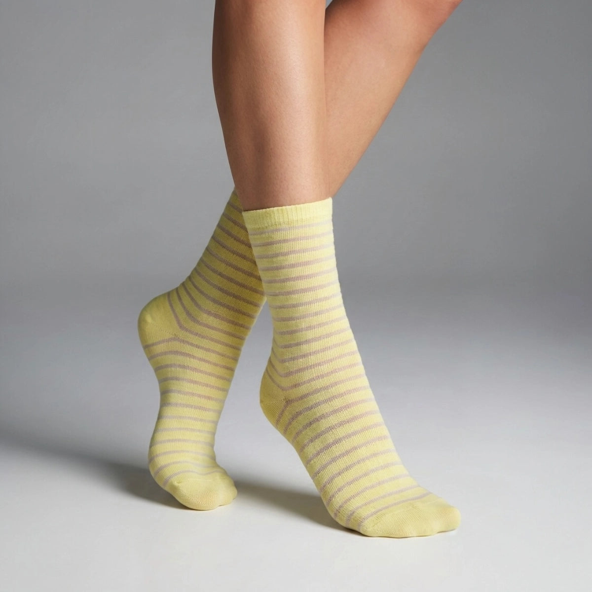 A Person wearing yellow socks with thin sheer stripes on a grey background