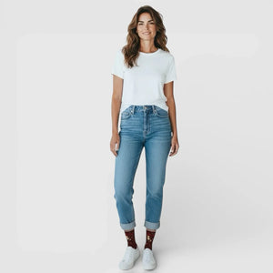 Woman wearing brown Christmas themed sox, in a white t-shirt and blue jeans on a plain background