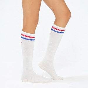 Woman wearing white knee-high socks with red and blue stripe on the cuff and the slogan 'you are not alone'