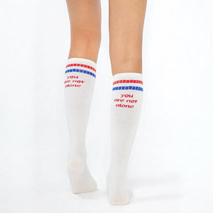 Woman wearing white knee-high socks with red and blue stripe on the cuff and the slogan 'you are not alone'