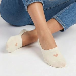 Person in jeans wearing a cream no-show sock with a beige heart design on a light grey background