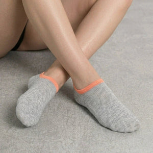 Person wearing grey no-seam ankle socks with orange cuff against a light background