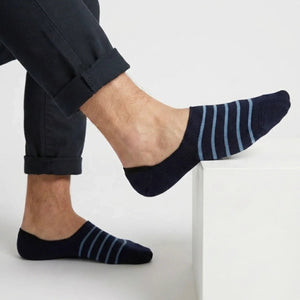 Navy with lighter blue stripe no-show socks worn with rolled-up dark pants on a light background
