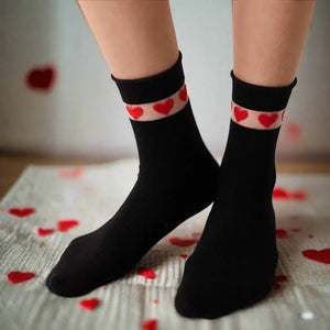 Woman's feet showing quarter length black socks with sheer cuff adorned with red love hearts, standing on a rug with red love hearts