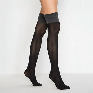 A woman in a gray top and thigh high black stockings poses confidently.