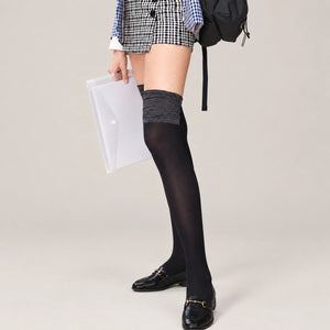 A woman in a gray top and thigh high black stockings poses confidently.