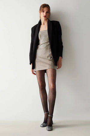 Woman wearing a black blazer, beige dress, and black tights with diamond line detail against a white background