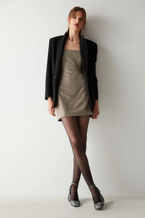 Woman wearing a black blazer, beige dress, and black tights with diamond line detail against a white background