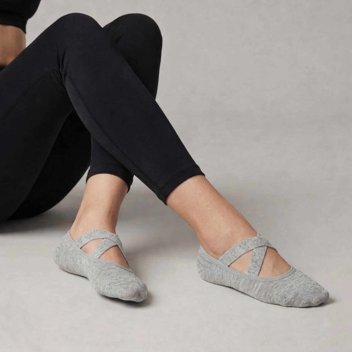 Person wearing grey yoga socks with crisscross straps and black leggings on a neutral background
