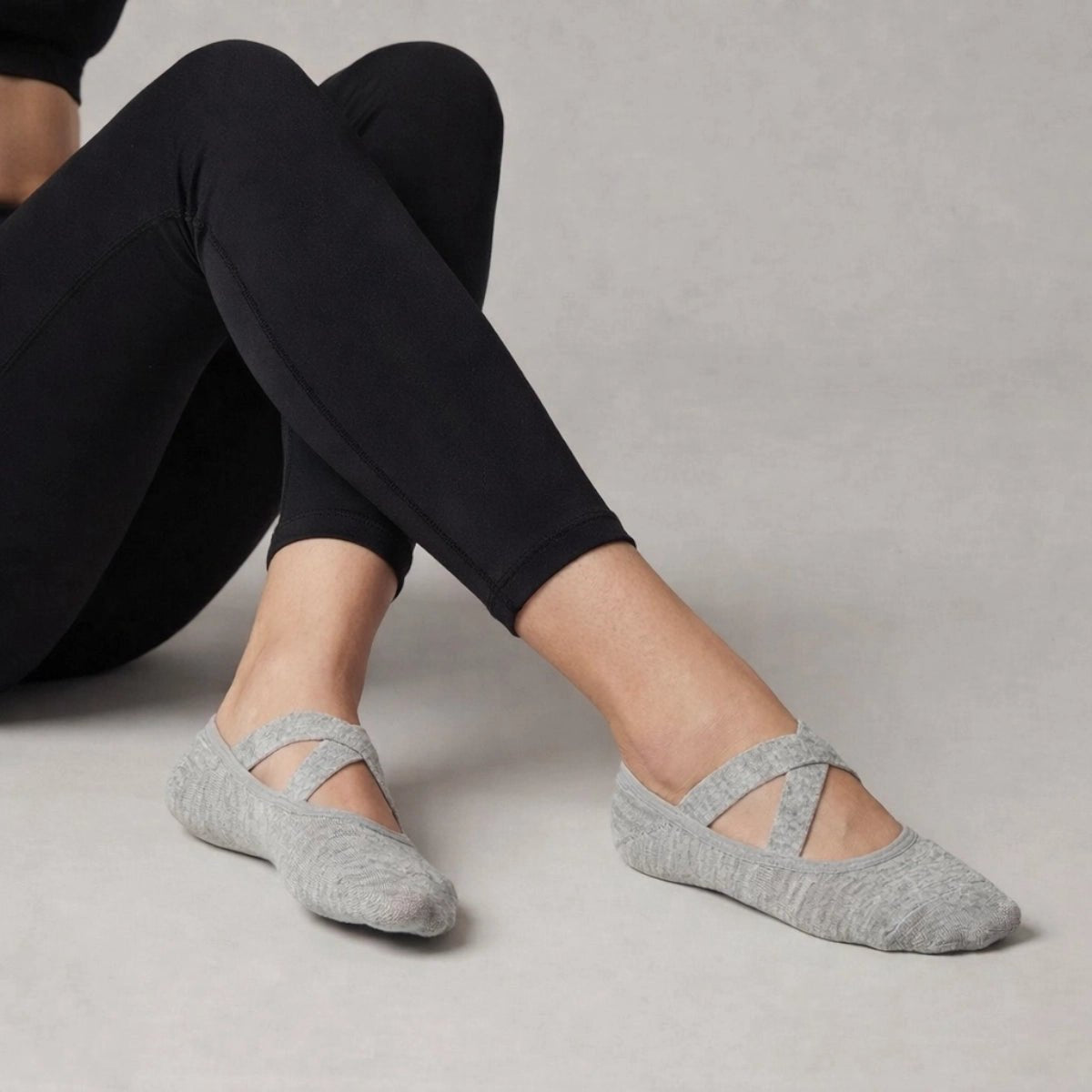 Person wearing grey yoga socks with crisscross straps and black leggings on a neutral background