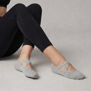 Person wearing grey yoga socks with crisscross straps and black leggings on a neutral background