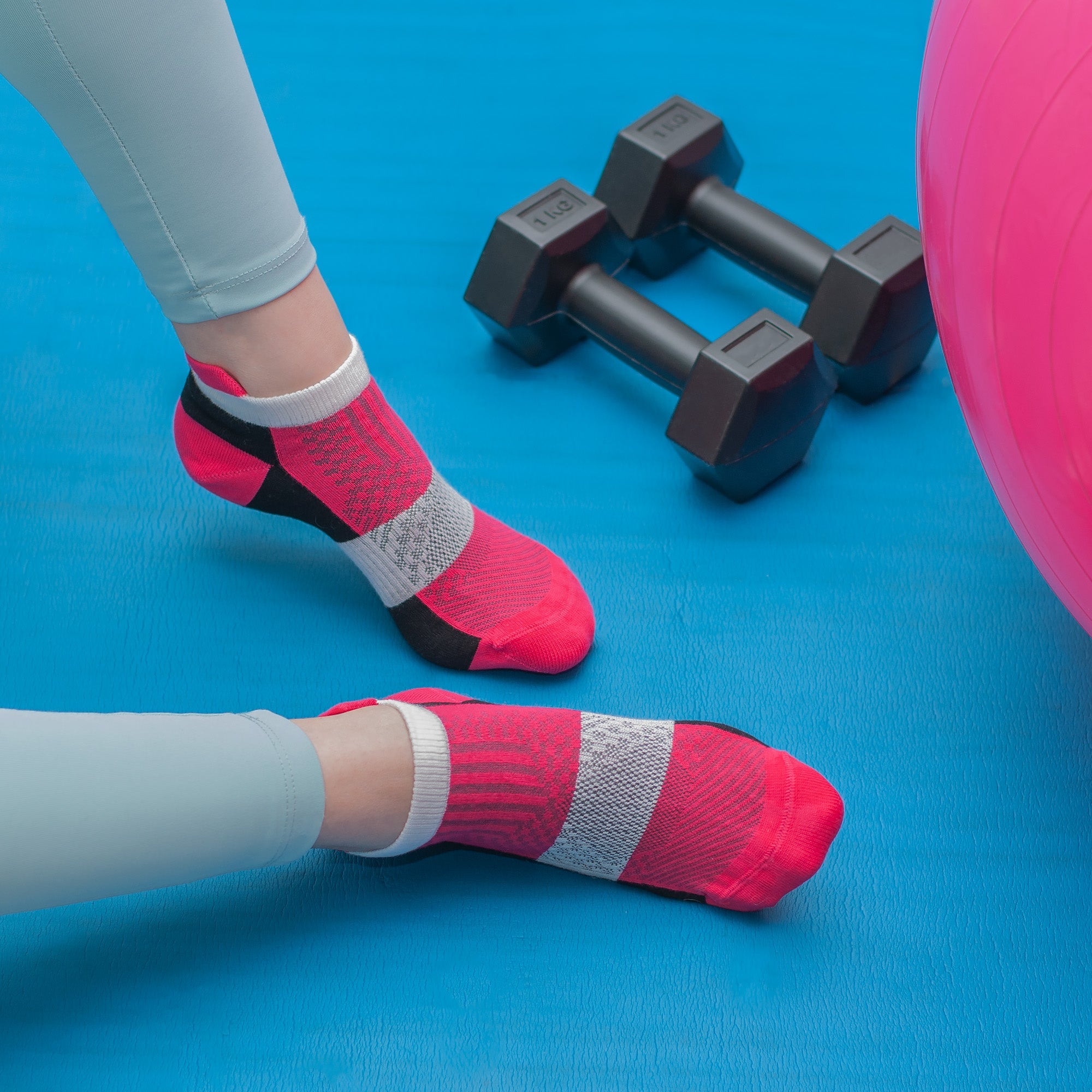 Photo of a person's legs wearing grey leggings and pink, grey, and black sneaker socks against a blue background
