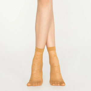 A pair of legs in tan nude socks with dots, emphasizing a chic and relaxed aesthetic.