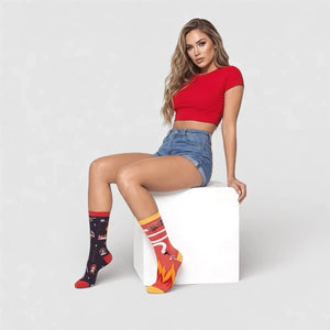 Model sitting on a white cube wearing Uniq Socks mismatched navy and red firefighter theme crew socks.