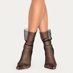 Women's black sheer mesh ankle socks with a subtle silver shimmer and a loose, slouchy fit on model's legs.