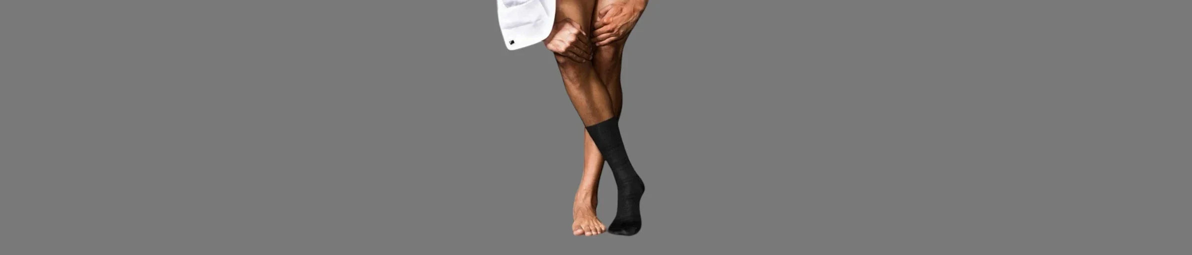 Bottom half of naked man's legs wearing a grey dress sock on right foot against a grey background