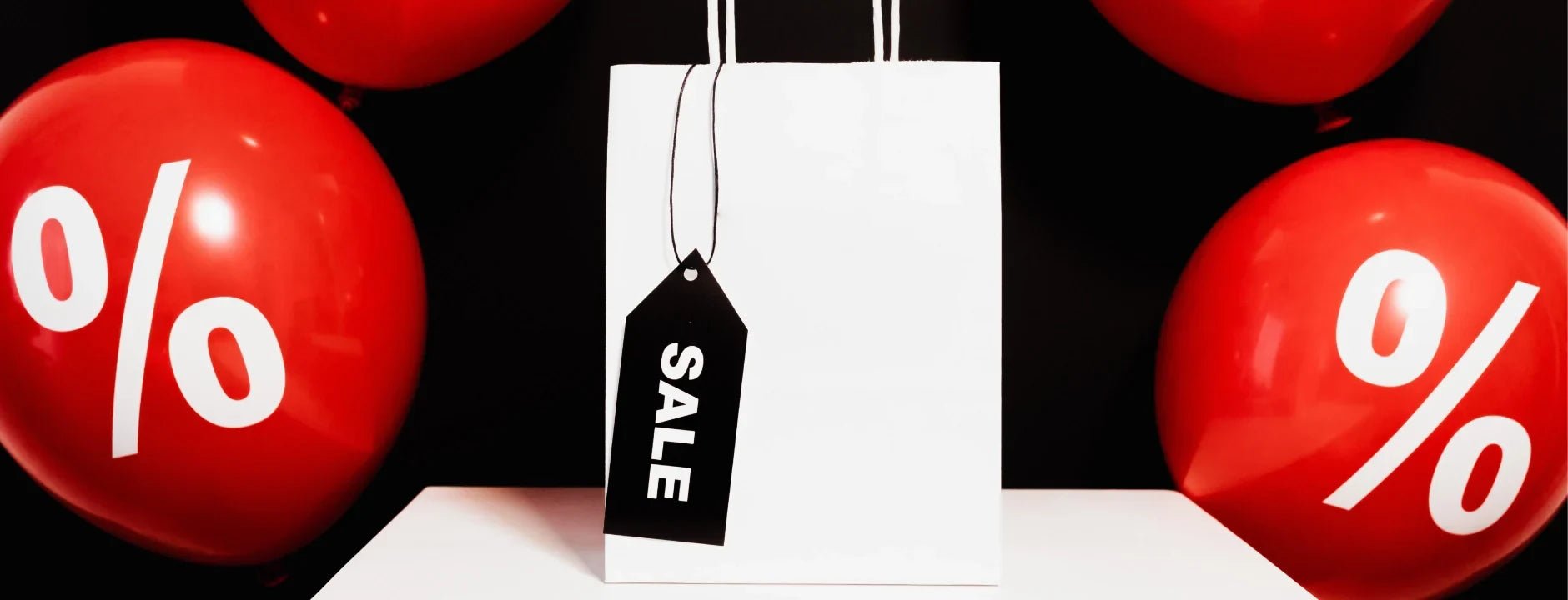 A white paper carrybag with a black 'Sale' tag and red balloons with whithe % sign