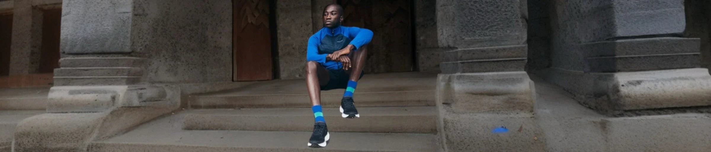 A man in a blue sports outfit sitting on the steps of a grey building
