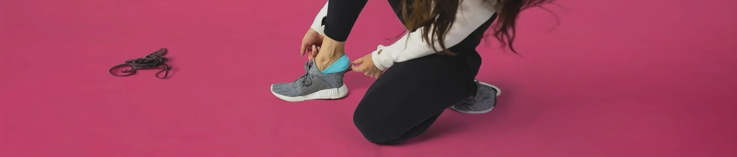 a woman wearing aqua no-show socks in sneakers against a pink background