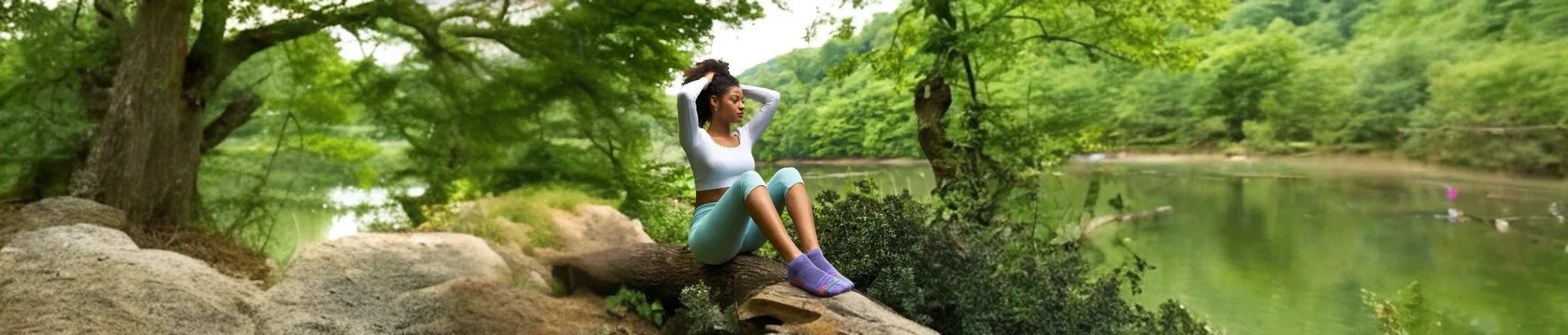 A woman in activewear and purple sneaker socks sitting in nature beside a river