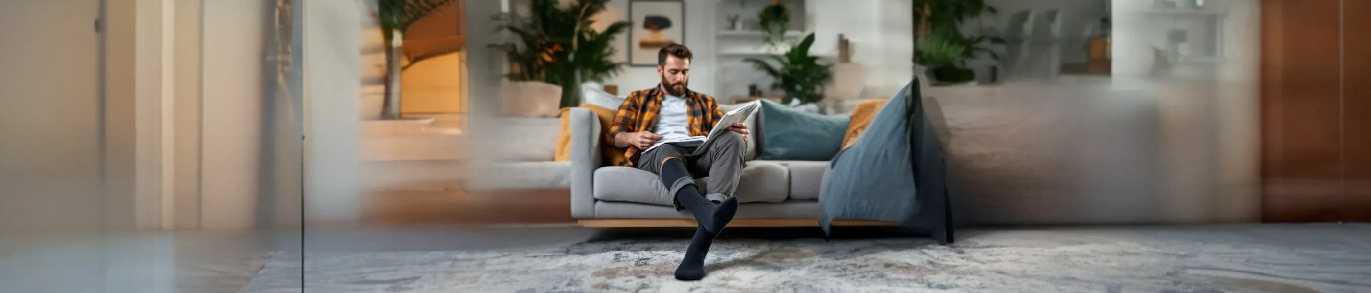 Man wearing crew socks reading a newspaper sitting on a grey lounge in a living room