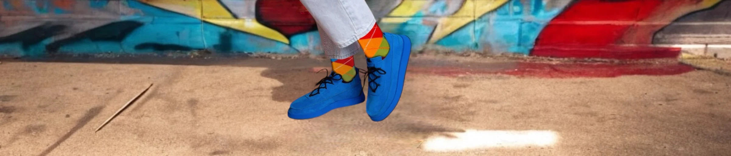 A person wearing multicoloured checkered socks and blue sneakers on a footpath in front of a graffiti wall