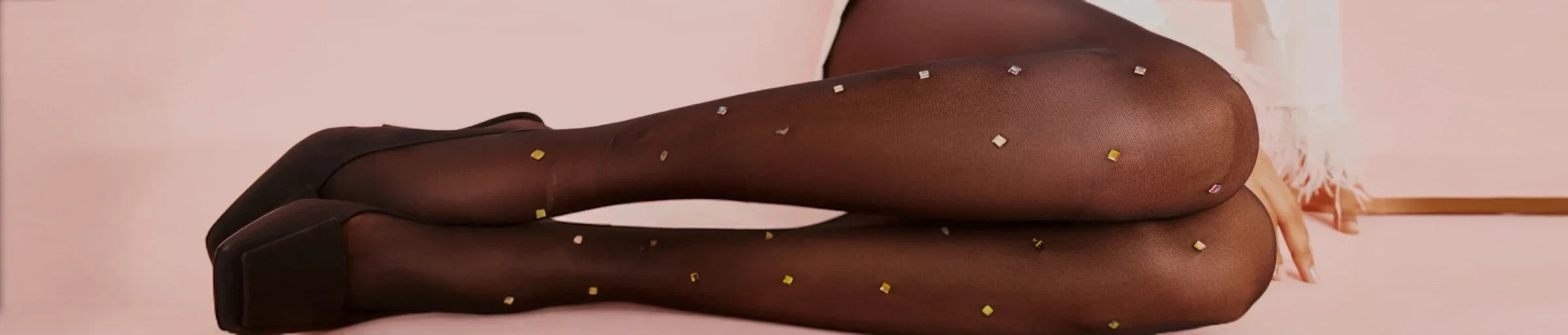 Bottom half of the legs of a woman lying down wearing sheer black tights with gold coloured crystals