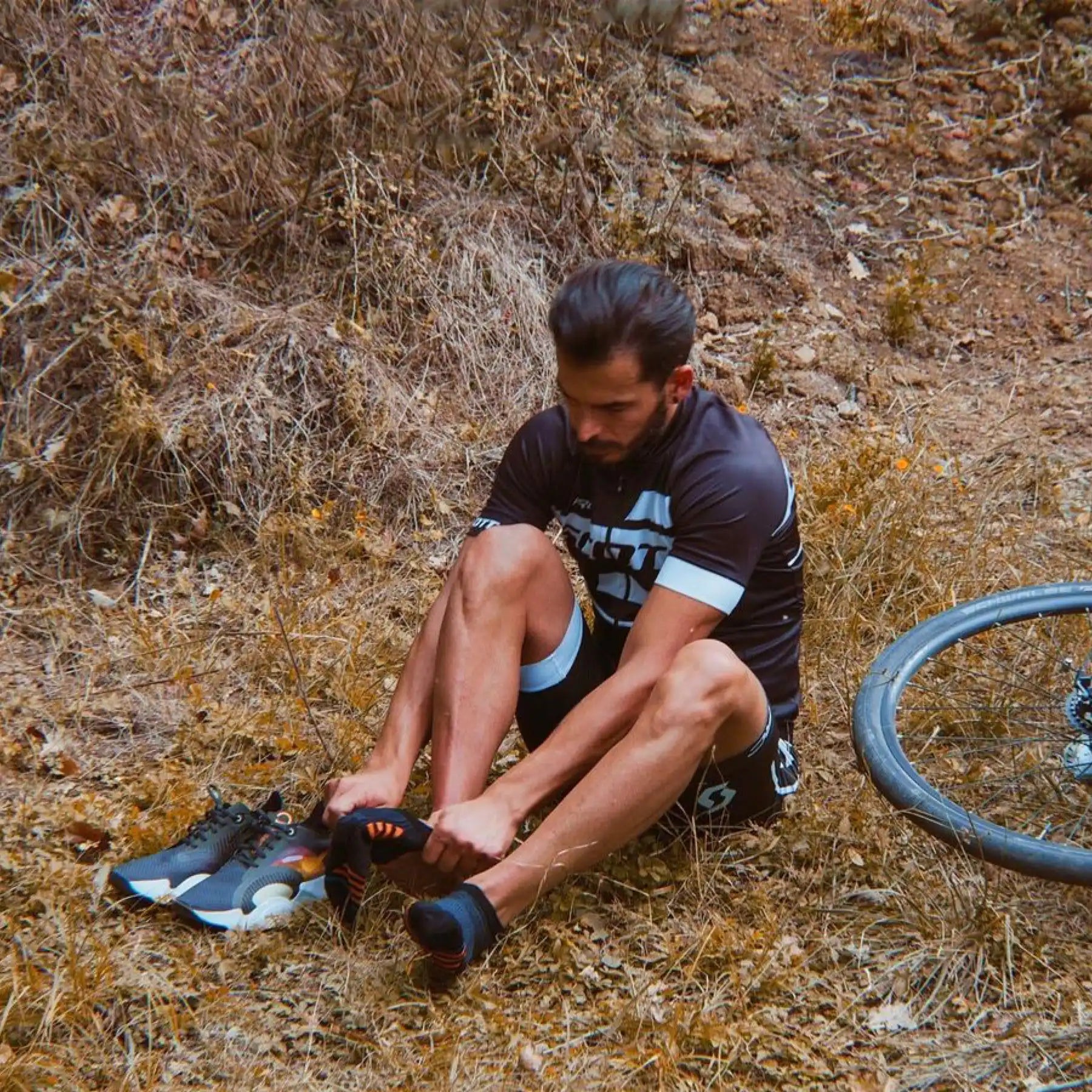 man on the ground putting on socks next to his bike