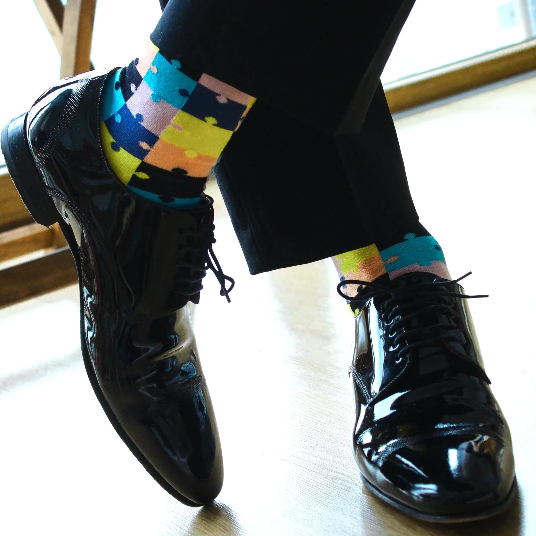 man wearing multicoloured puzzle themed socks and black leather shoes