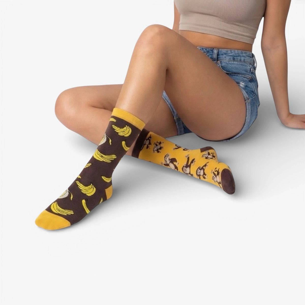 Person wearing mismatched brown socks with monkey and banana patterns on a white background